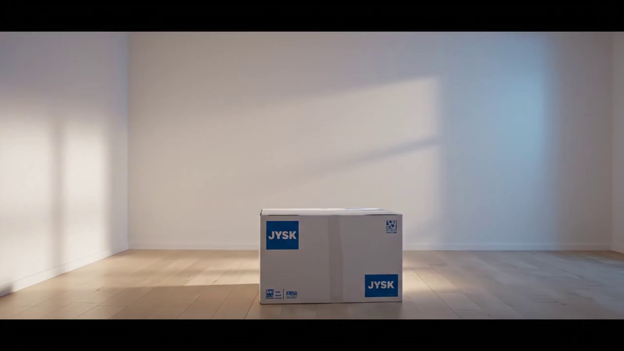 Cinematic shot of a sunlit Scandinavian bedroom. A sealed JYSK box trembles, opens, and flat pack furniture assembles rapidly into a serene, styled room highlighted by a yellow JYSK throw on the bed. - Veo 3 AI video prompt thumbnail