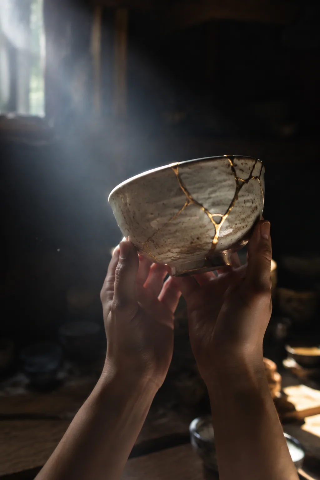 Vertical video still: the same bowl, now repaired with gold seams, held up into a shaft of light.