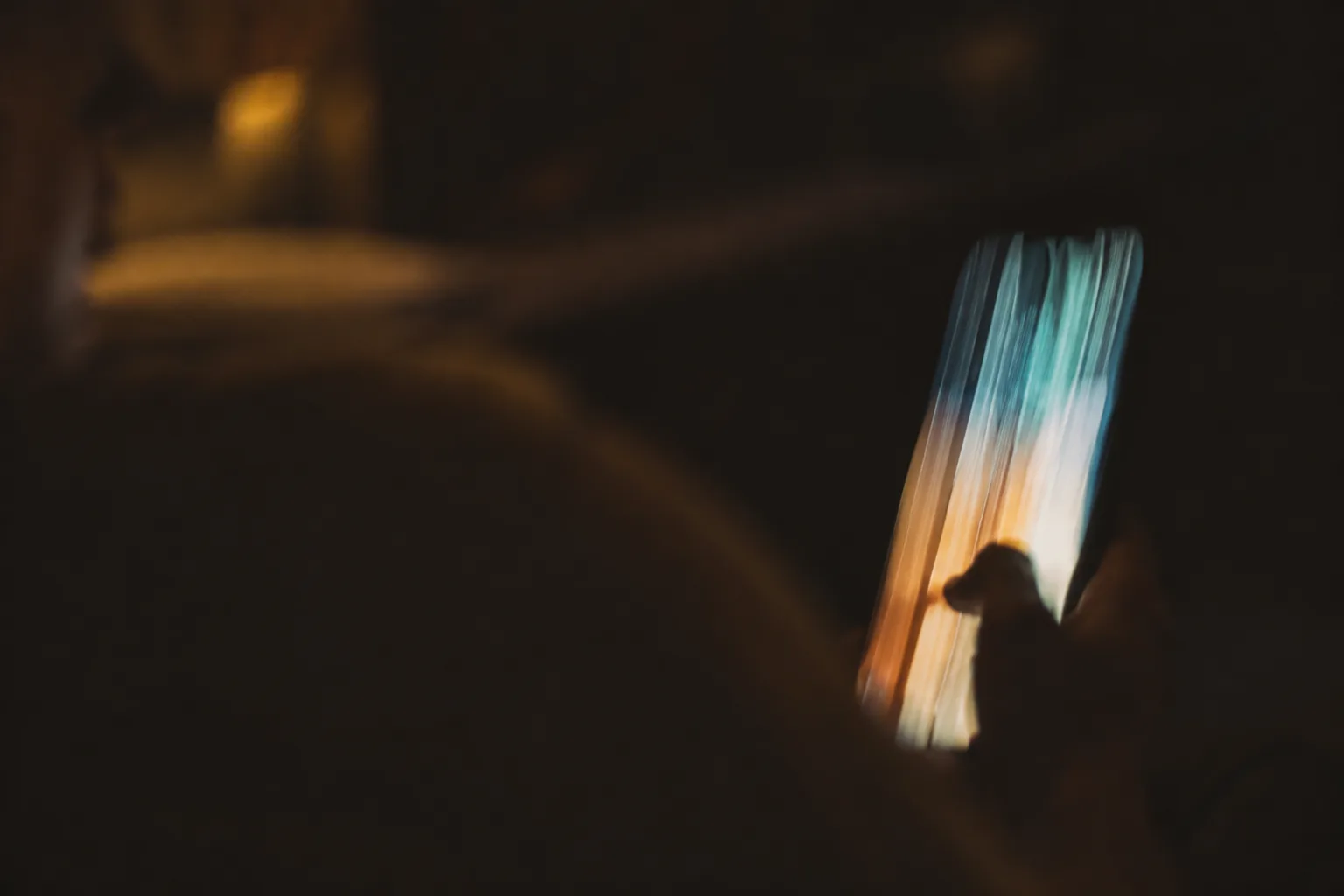 A phone screen smeared into motion blur mid-swipe, glowing teal and amber in a dark room.